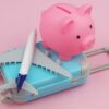 A pink piggy bank, suitcase and plane on a plain pink background