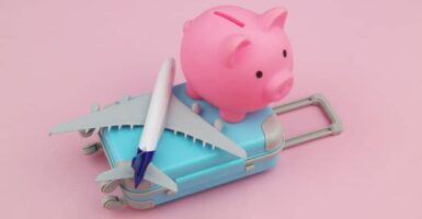 A pink piggy bank, suitcase and plane on a plain pink background