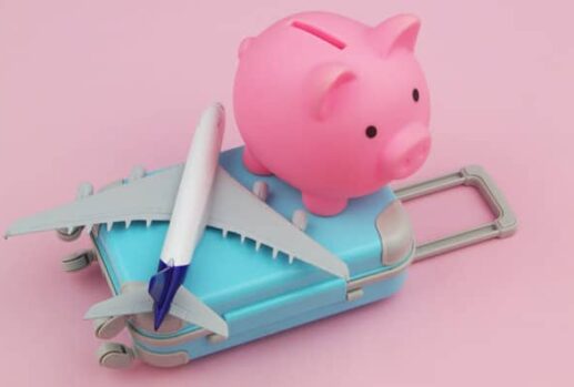 A pink piggy bank, suitcase and plane on a plain pink background