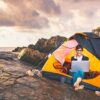 Girl working on laptop sitting in a tent on a cliff top