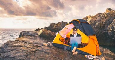 Girl working on laptop sitting in a tent on a cliff top