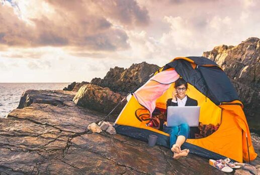 Girl working on laptop sitting in a tent on a cliff top